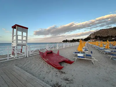 a sandy beach with chairs and a lifeguard tower at Casa Vacanza Mondello nel Cuore in Mondello