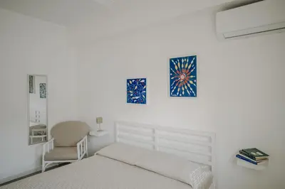a white bedroom with a bed and a chair at La Perla d'Argento in Santa Flavia