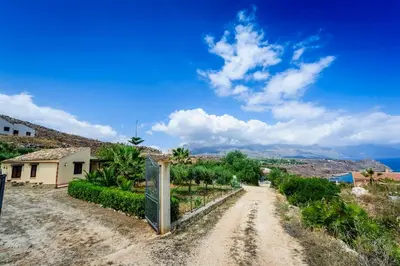 a dirt road in front of a house and the ocean at Villa del Carrubo in Castellammare del Golfo in Castellammare del Golfo