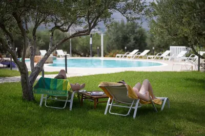 two people laying in lawn chairs next to a pool at Casale La Macina - Hotel, Scopello in Scopello