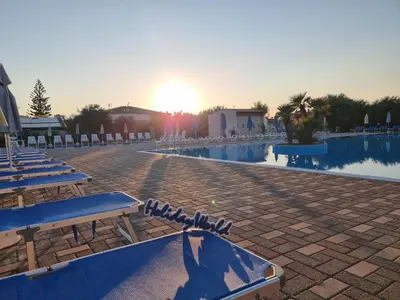 a resort with a pool with chairs and the sunset at Respiro di Mare by Holiday World in Buonfornello