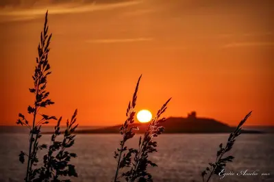 a sunset over the water with a lighthouse in the background at Caterina in Isola delle Femmine