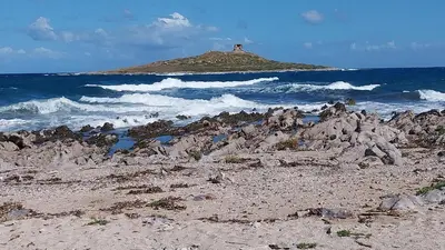 a beach with rocks and the ocean with a lighthouse at Caterina in Isola delle Femmine