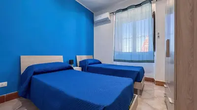 a blue room with two beds and a window at Appartamento Cinisi in Cinisi