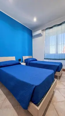 a blue room with three beds and a window at Appartamento Cinisi in Cinisi
