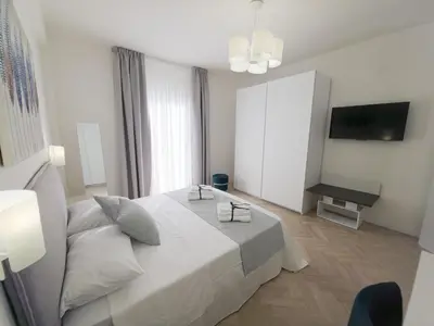 a white bedroom with a large bed and a television at Light Charme, Natural Light Apartment a due passi dalla PIAZZA DUOMO in Terrasini