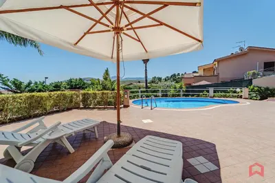 a patio with chairs and an umbrella and a pool at Delizioso Appartamento in villa & Piscina Privata in Trabia