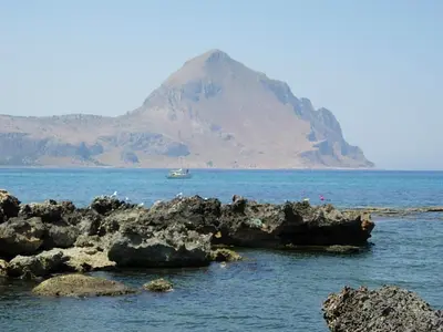 a mountain in the ocean with a boat in the water at Aquilone in Castelluzzo