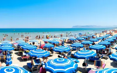 a beach with blue umbrellas and crowds of people at Stella Del Mare in Castellammare del Golfo