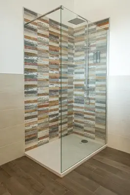 a shower with a glass wall and wood panels at kalispera in Cinisi