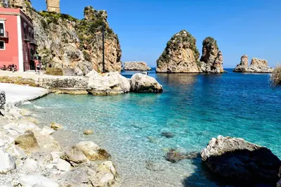 a beach with rocks in the water and a pink building at Casa vacanze CaMi in Alcamo