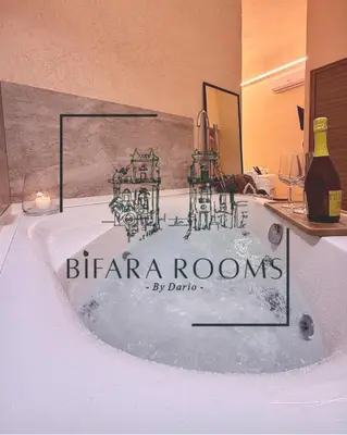 a bath tub with a candle and a bottle of wine at Bìfara Rooms in Palermo