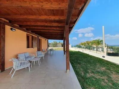 a covered patio with chairs and a table and a lawn at Apartment MareLuce by Interhome in Balestrate