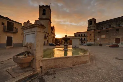 a fountain in the middle of a courtyard with a church at Casetta in piazza in Palazzo Adriano