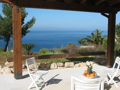 a table and chairs on a patio with a view of the ocean at Agave Scopello in Scopello
