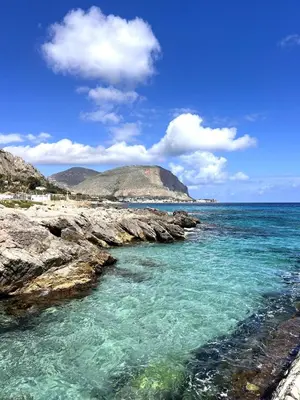 a beach with blue water and a rocky shore at Nuovo appartamento sul mare immerso nel verde in Palermo