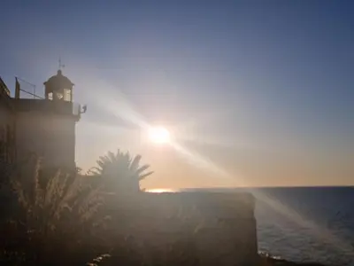 a lighthouse on the ocean with the sun in the sky at Luxury apartment Villa Vera Mondello - Palermo in Mondello