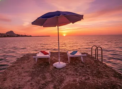 two chairs under an umbrella on the beach at sunset at Sunset in Santa Flavia