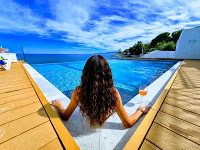a woman sitting next to a swimming pool with a glass of wine at White Coral in Santa Flavia