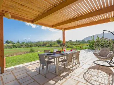 a patio with a table and chairs under a wooden pergola at Villa Aura Scopello in Castellammare del Golfo