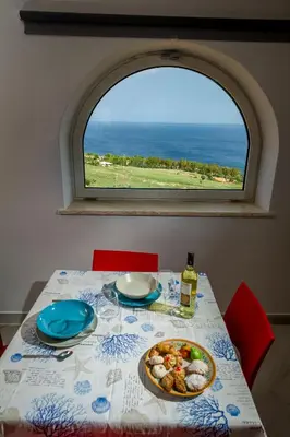 a table with a plate of food and a window at APT NINO in Villa Rosaria Vista Mare Zingaro in Scopello