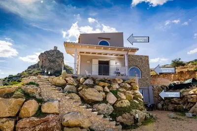 a house on top of a mountain with a rock wall at APT Marta in Villa Rosaria Vista Mare Zingaro in Scopello
