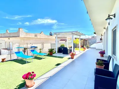 a patio with blue chairs and grass at Villa dei Gerani, a 500 mt dal mare in Alcamo