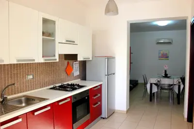 a kitchen with red cabinets and a sink and a table at Appartamento Calvino piano terra in via Mulino 31 in San Vito lo Capo