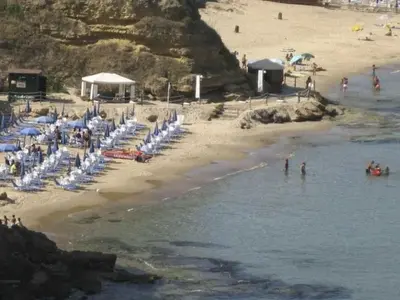 a beach with a bunch of chairs and people in the water at Apartment Lila Wohnung mit Schwimmbad und Meerblick by Interhome in Balestrate