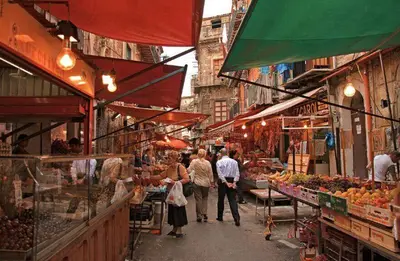 a group of people walking through an outdoor market at Auri's home in Palermo