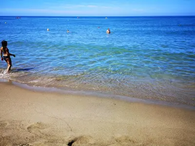 a person walking on the beach with people in the water at Holiday Home Helle mediterrane Villa mit Veranda und Garten by Interhome in Cefalù