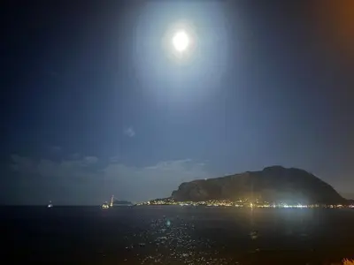 a moon rising over a mountain in the ocean at night at Chiaro di luna holiday in Palermo