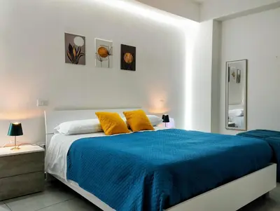 a white bedroom with a blue bed with yellow pillows at Aria di Paese in Altavilla Milicia