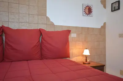 a red bed with red pillows and a table with a lamp at Appartamenti da Clarissa in Macari