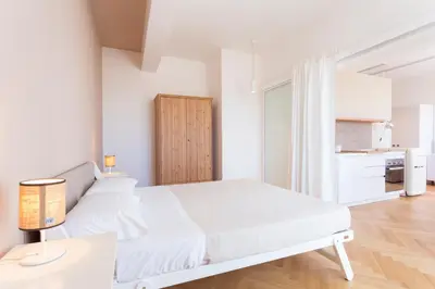 a white bedroom with a white bed and a kitchen at Residence Itaca in Castellammare del Golfo