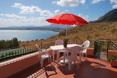 a table and chairs on a balcony with a red umbrella at Casa Vacanze La Terrazza Sul Golfo in Castellammare del Golfo