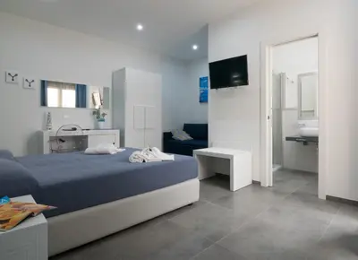a bedroom with a blue bed and a bathroom at Pharos in San Vito lo Capo