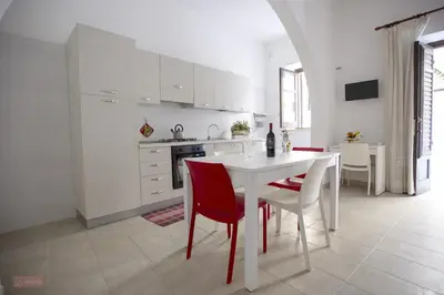 a white kitchen with a white table and red chairs at Le Gemme di Sicilia Apartments in Castellammare del Golfo