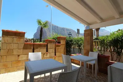 a patio with tables and chairs and mountains in the background at B&B Villa Bea in San Vito lo Capo