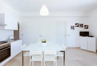 a white kitchen with a table and white chairs at Residence Guidaloca in Scopello