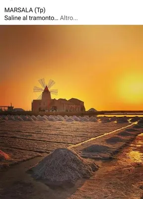 a beach with a windmill in the sunset at Lomarchi Holiday Home in Carini