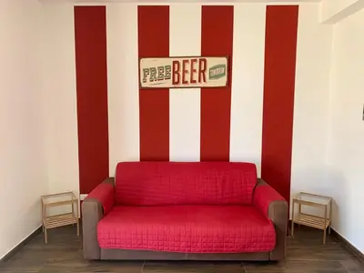 a red couch against a striped wall with a beer sign at Appartamento Il Pomodoro in San Vito lo Capo
