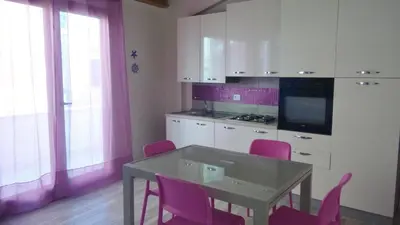 a kitchen with pink chairs and a table and a kitchen with white cabinets at La Perla Bianca in Castellammare del Golfo
