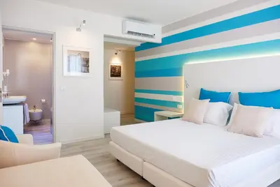 a bedroom with a white bed with blue and white stripes at Marina di Petrolo Hotel & SPA in Castellammare del Golfo