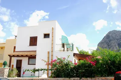a white house with a balcony and mountains in the background at Senia in San Vito lo Capo