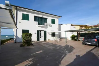a white house with a car parked in a parking lot at Dune Home alloggi sul mare in Alcamo Marina