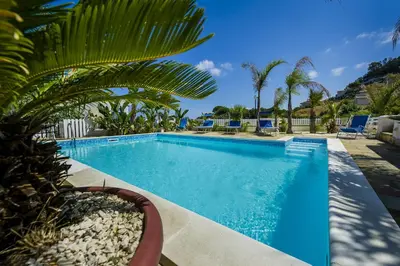 a swimming pool with palm trees and blue chairs at Villa Oleandro in Alcamo Marina