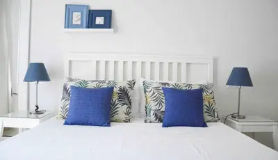a white bed with two blue pillows and two lamps at Villa Almyra in San Vito lo Capo