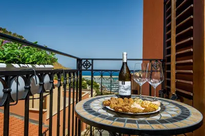 a table with a bottle of wine and wine glasses on a balcony at Antico Canale in Castellammare del Golfo