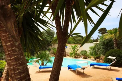a swimming pool with blue chairs and palm trees at Villa Sole in San Vito lo Capo